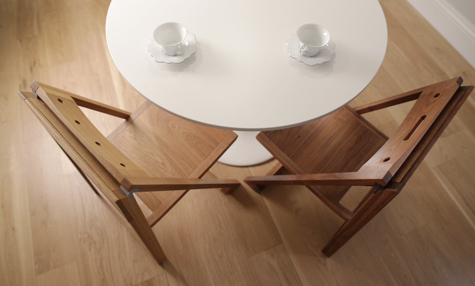 Two PicChair chairs at a round white table with two tea cups. A wooden floor is below.